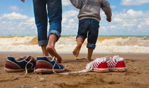 Deux paires de soulier sur la plage, l'une appartenant à une adulte et l'autre à un enfant, avec ces deux personnes qui marche vers l'océan